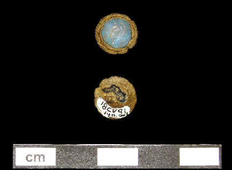 Blue faceted glass jewel in a copper alloy setting with a decorative crimped rim. 